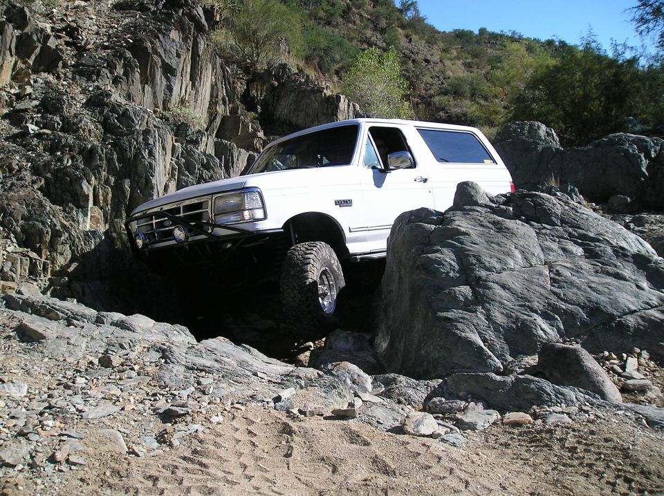 White Ford Bronco with aftermarket bumper and large tires navigating rocky terrain