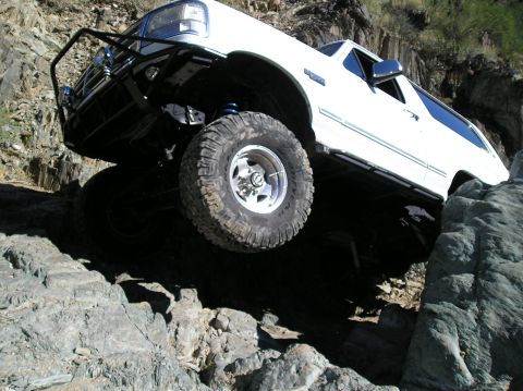 1993 Ford Bronco - White Ford Bronco navigating a rocky trail with its front tire lifted.