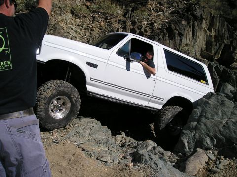 1993 Ford Bronco - A white Ford Bronco navigates a challenging rocky trail with a driver visible inside.