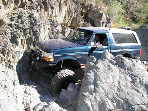 1993 Ford Bronco - A teal Ford Bronco maneuvers through a challenging rocky terrain, with another vehicle visible in the background.