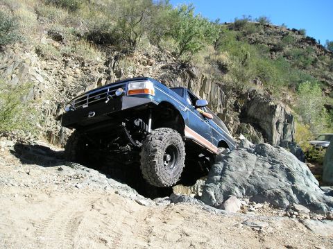 1993 Ford Bronco - A modified Ford Bronco navigates a rocky off-road trail under a clear blue sky.
