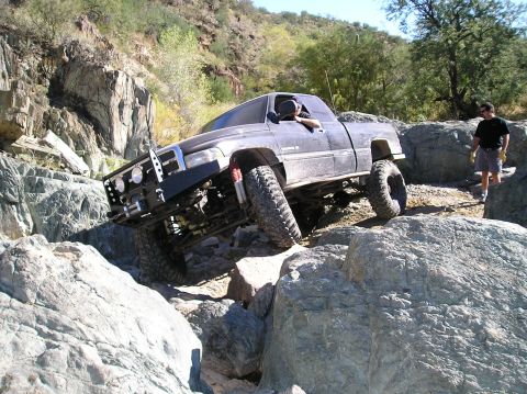 1993 Ford Bronco - A modified black pickup truck tackles a challenging rocky terrain, demonstrating its off-road capabilities.