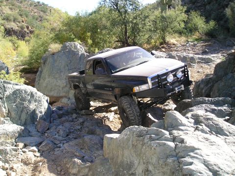 1993 Ford Bronco - A lifted Dodge Ram pickup truck is shown navigating a challenging rocky terrain in a desert environment.