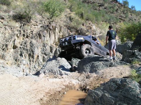 1993 Ford Bronco - A black pickup truck is shown traversing a challenging rocky terrain on an off-road trail.