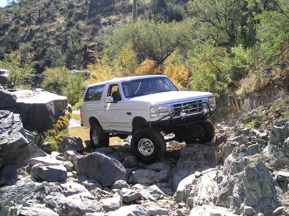White lifted Ford Bronco with tube bumper crawling over boulders in a desert wash