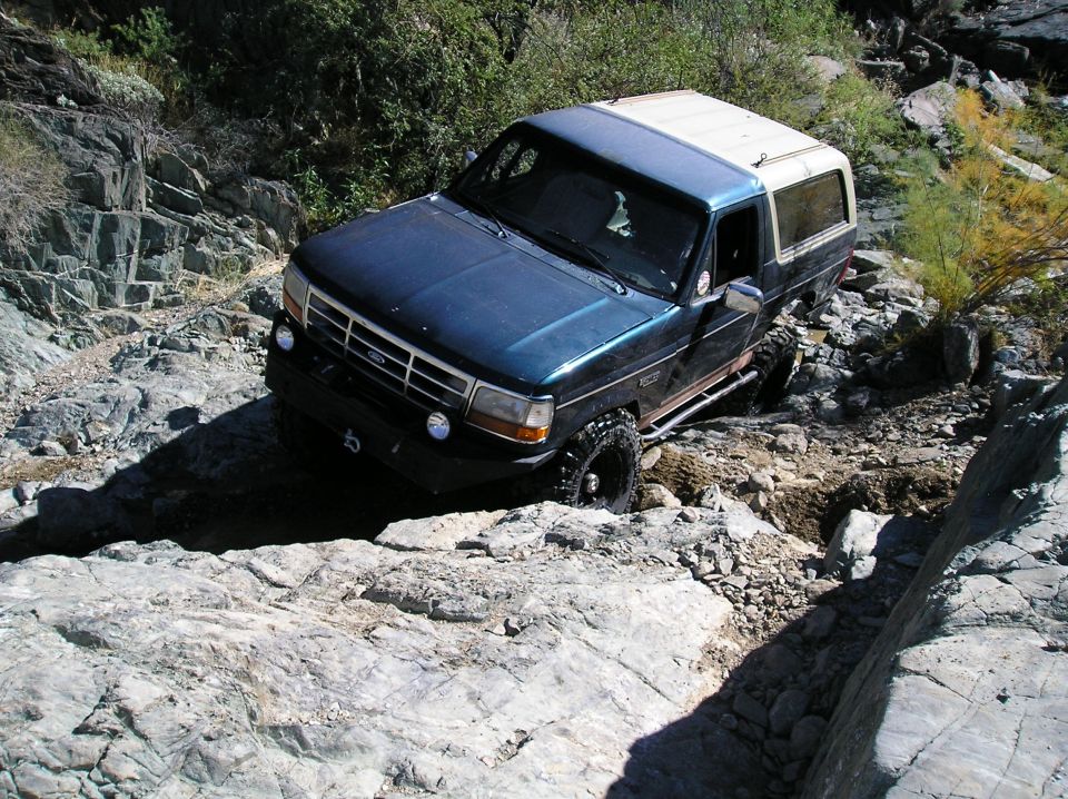 Dark green Ford Bronco with white top navigating a rocky trail