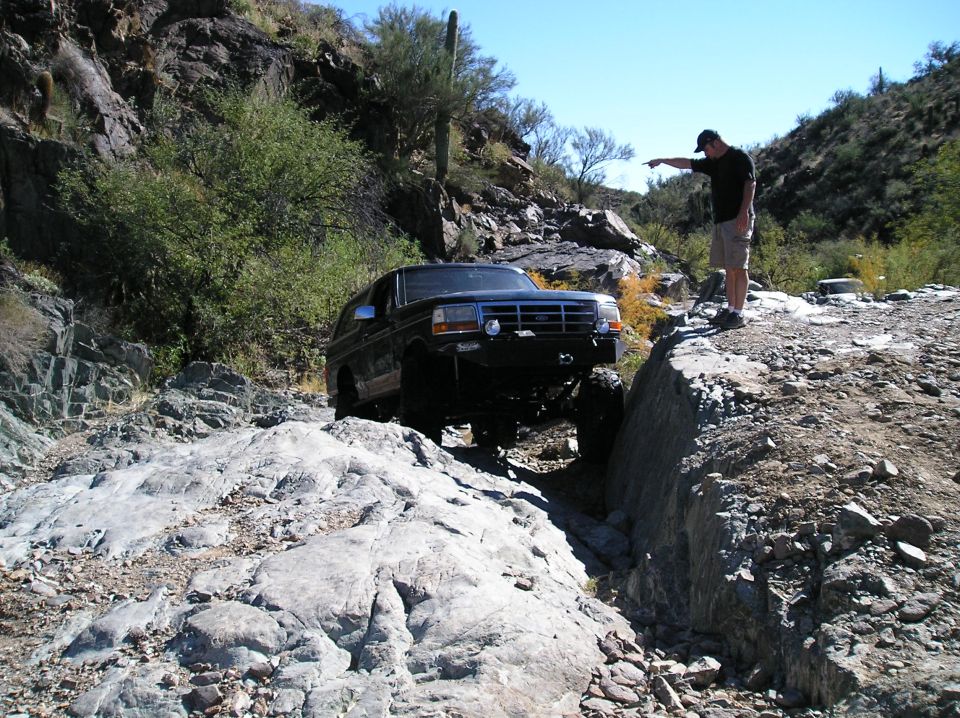 Dark blue Ford Bronco navigating a rocky, off-road trail with a man pointing