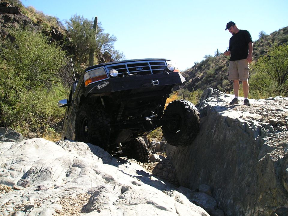 Dark green lifted Ford Bronco flexing into a rock crevice with spotter watching
