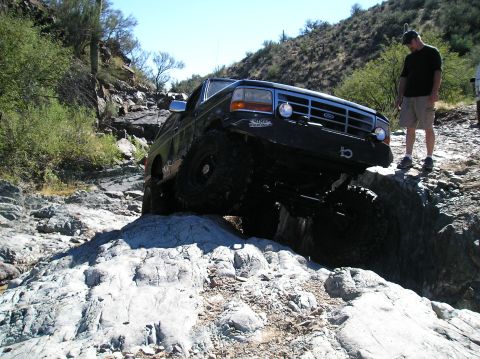 1993 Ford Bronco - A modified Ford Bronco tackles a challenging rocky terrain on a sunny day.