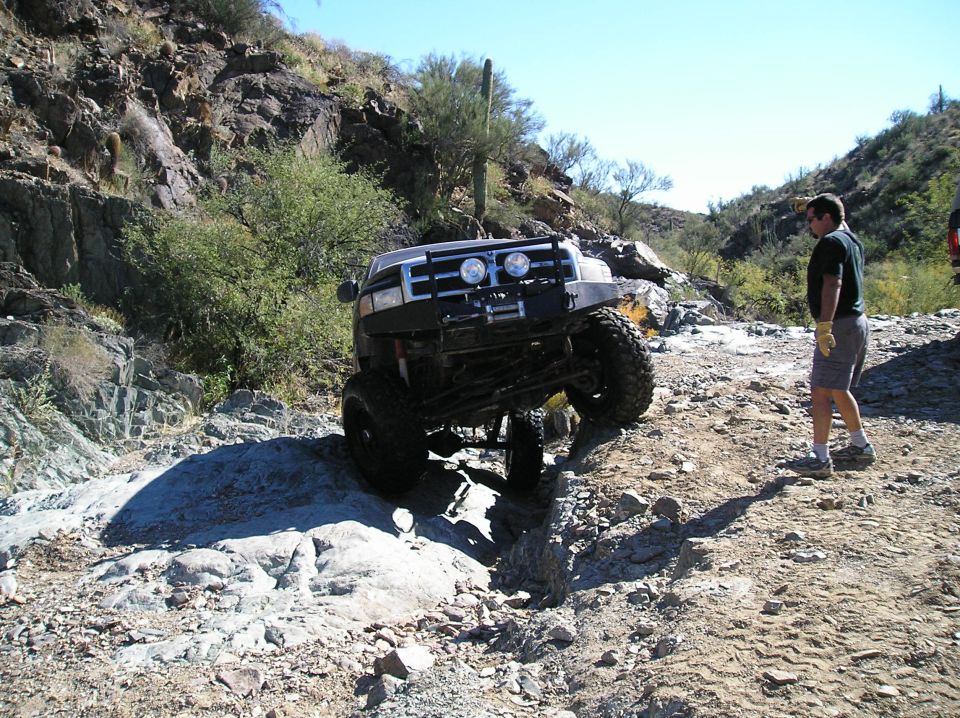 Silver off-road SUV with large tires navigating a rocky trail, front bumper and grille visible