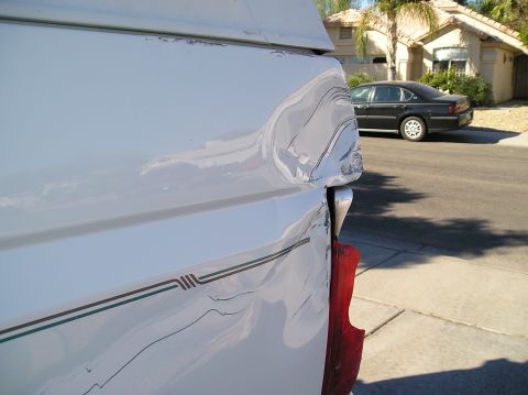 1993 Ford Bronco - Close-up of a damaged white pickup truck bed, with a black sedan visible in the background.