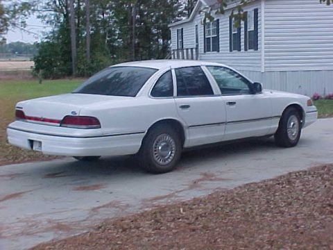 1993 Ford Crown Victoria - A white 1993 Ford Crown Victoria sedan is parked on a concrete driveway in front of a house.