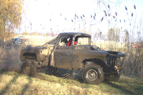 1978 Ford Bronco - A 1950s Chevrolet Task Force stepside pickup, cab and bed thickly coated in drying mud, powers through a grassy field with mud flying off t…