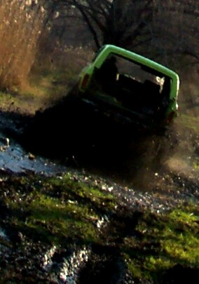 1978 Ford Bronco - Motion-blurred rear shot of a bright green doorless 4x4 with an open rear cab and roll bar running away from the camera through a muddy two…