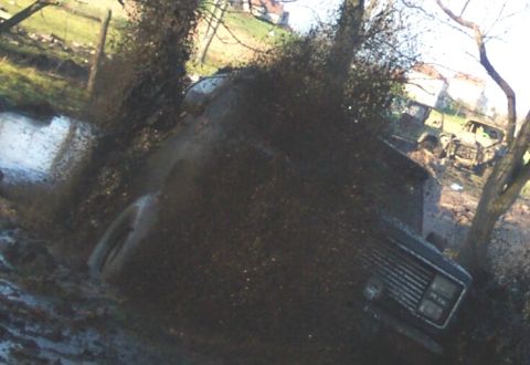 1978 Ford Bronco - A dark 4x4 blasts through a mud hole and hurls a sheet of mud directly at the camera lens, obscuring most of the frame with flying muck and…