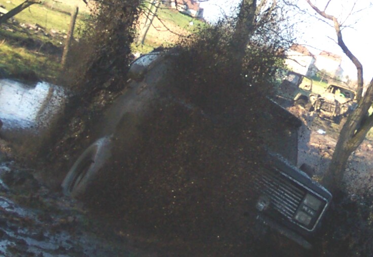 Mud sprayed across the camera as a dark 4x4 blasts through a mud hole