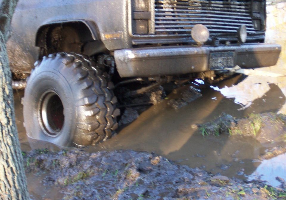 Front corner of a square-body 4x4 in a mud hole with a tall lug off-road tire