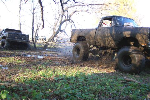 1978 Ford Bronco - Two mud-covered trucks are engaged in off-road activity in a wooded area.