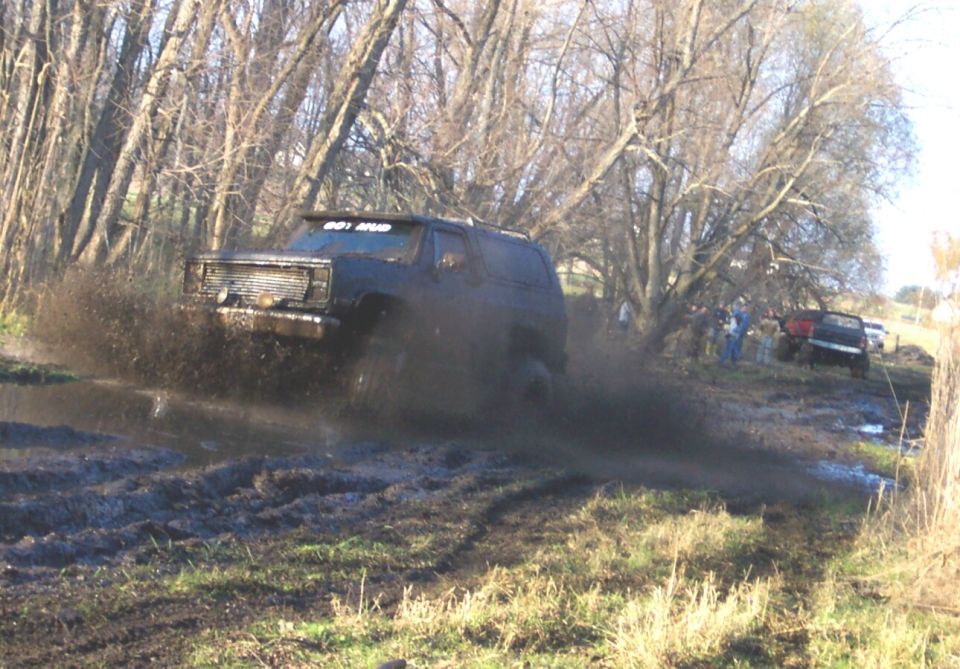 Dark square-body Blazer SUV with GOT MUD banner blasting through a mud pit