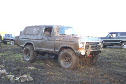 1978 Ford Bronco - A full-size Ford Bronco coated bumper to roof in drying tan mud sits in a churned field, wearing a tube front bumper stuffed with grass and…