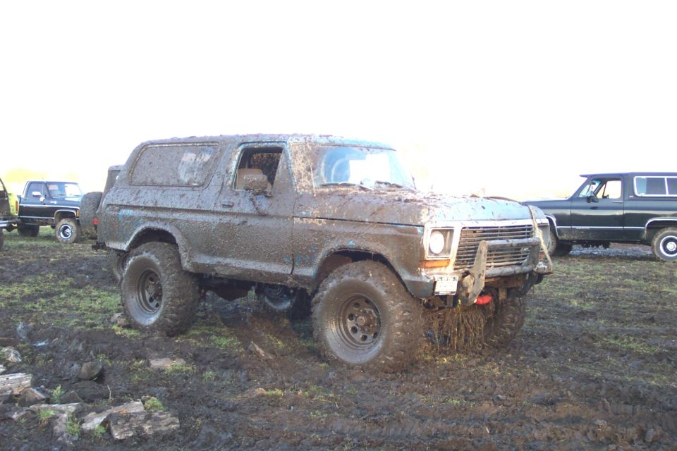 Ford Bronco caked in tan mud with tube bumper and black steel wheels in a field