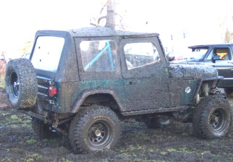 1978 Ford Bronco - A mud-splattered Jeep CJ-7 navigates a muddy terrain, with another vehicle visible in the background.
