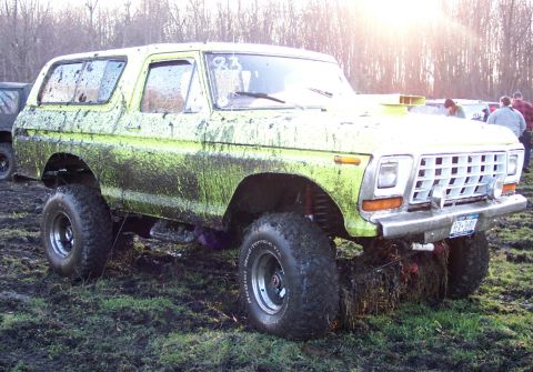 1978 Ford Bronco - This lifted Bronco is covered in mud, suggesting it has been used for off-roading. A second vehicle is partially visible in the background.