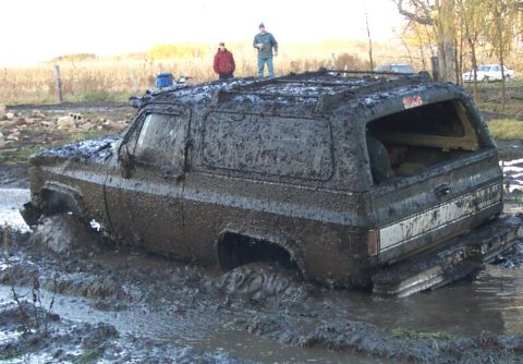 1978 Ford Bronco - Rear three-quarter view of a square-body Chevrolet Blazer/K5-style two-door SUV buried to the rocker panels in a mud hole, its entire body…
