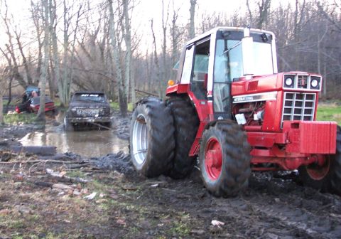1978 Ford Bronco - A red International Harvester farm tractor with dual rear tires and a front weight bracket sits in churned mud, apparently on recovery duty…