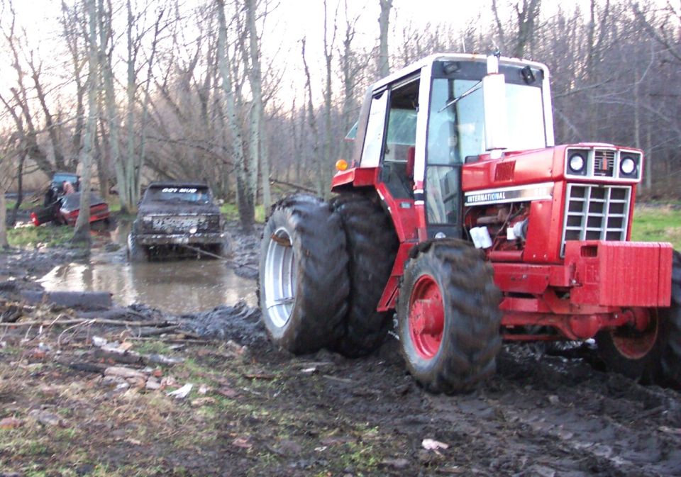 Red International Harvester tractor with duals in the mud beside a stuck pickup