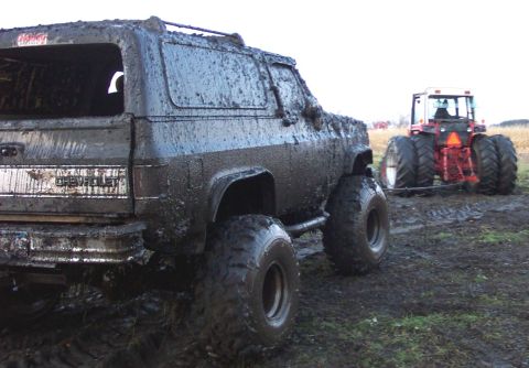1978 Ford Bronco - A heavily mud-caked SUV is being towed by a tractor in a muddy field.