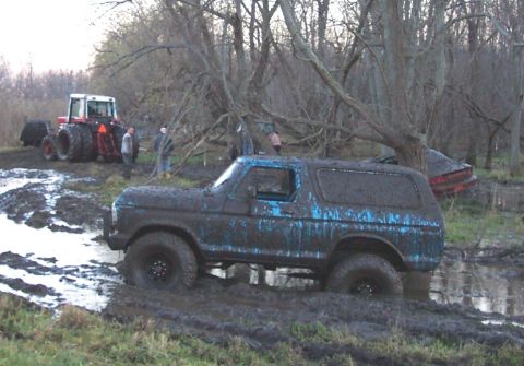 1978 Ford Bronco - Side view of a lifted blue full-size Ford Bronco with a removable hardtop sitting in a rutted mud bog, its body coated in a thick layer of…