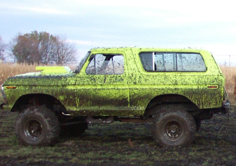 Lime-green full-size Ford Bronco side profile, covered in mud in a field