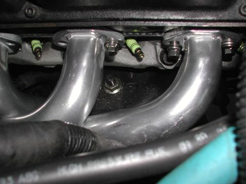 1993 Ford Thunderbird - Close-up view of an engine's exhaust manifold and spark plugs, with some visible part numbers on a hose.