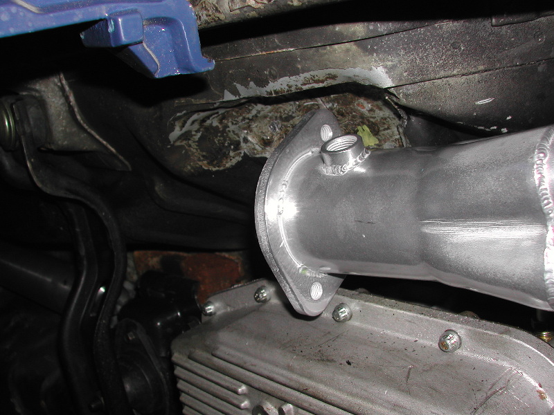 Close-up of an exhaust pipe flange bolted to a silver engine component, with blue bracketry above