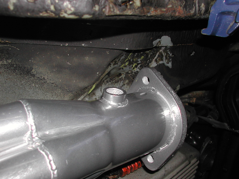 Close-up of a silver exhaust pipe flange with a threaded fitting