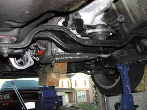1993 Ford Thunderbird - Vehicle underside with suspension and exhaust parts visible, supported by jack stands. A GMC truck is in the background.
