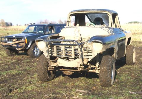1978 Ford Bronco - Two off-road vehicles are parked in a muddy field under a cloudy sky.