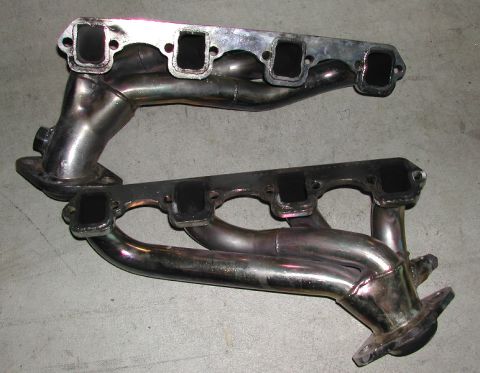 1993 Ford Thunderbird - A pair of exhaust manifolds are shown, one with a polished finish and the other with a matte black coating.