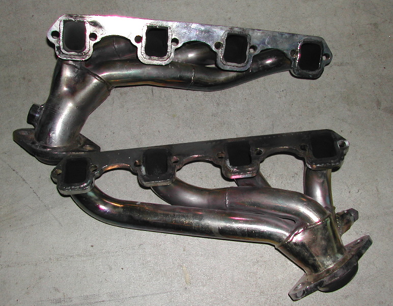 Two exhaust manifolds on a gray surface. One is shiny, the other is darker