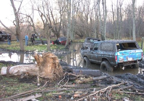 1978 Ford Bronco - Several vehicles, including a 1978 Ford Bronco, are stuck in the mud in a wooded area.