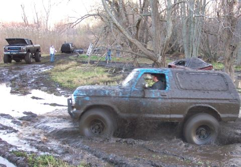 1978 Ford Bronco - A muddy 1978 Ford Bronco navigates a challenging off-road course with other vehicles in the background.