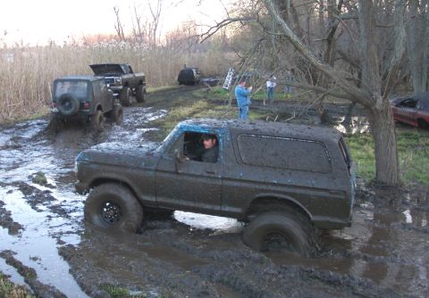 1978 Ford Bronco - Several vehicles navigate a muddy off-road course, with one Bronco deeply stuck in the mire.