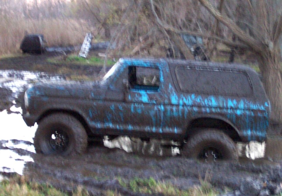 Mud-covered 1978 Ford Bronco in a muddy field, side view