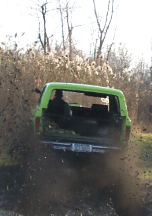 1978 Ford Bronco - A green SUV kicks up mud as it drives through a muddy area, with a watermark for SUPERMOTORS.NET visible.