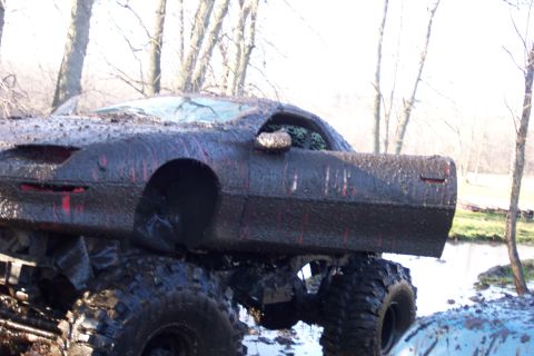 1978 Ford Bronco - Close 3/4 rear view of a red sport coupe body, plastered in thick gray mud with red paint streaking through, riding high on a lifted 4x4 ch…