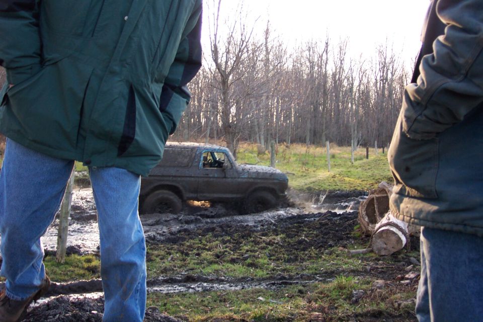 Muddy SUV stuck in a muddy field with two people watching