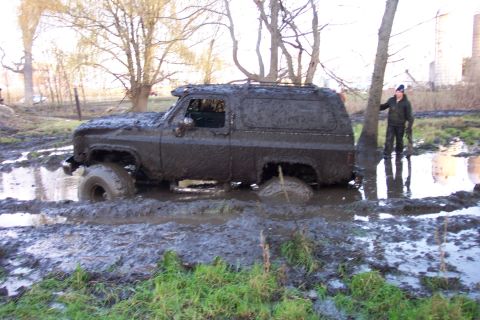 1978 Ford Bronco - A mud-covered SUV is stuck in a muddy field, with a person observing the scene.