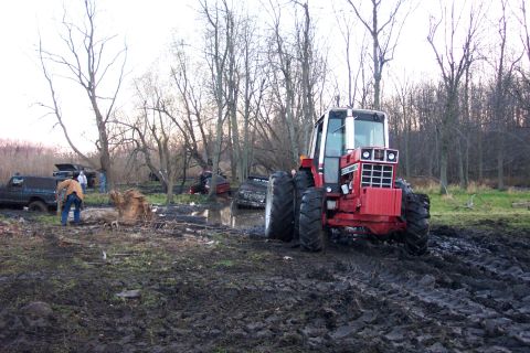 1978 Ford Bronco - A red International Harvester cab tractor on dual rear tires and front-wheel-assist axles pulls out of a churned mud pit at a backyard mud-…