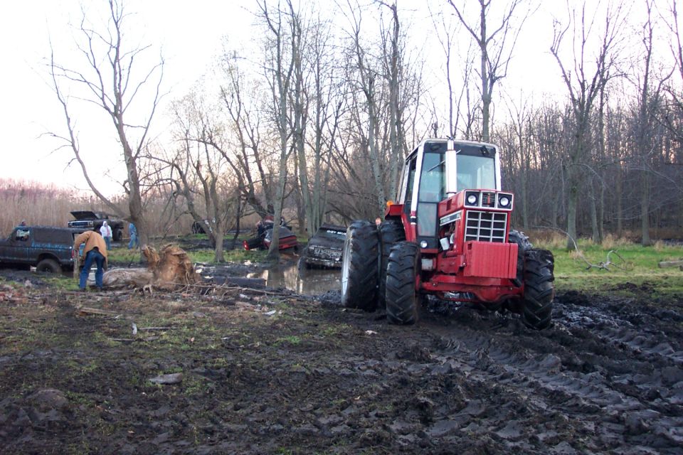 Red International Harvester tractor with dual tires pulling out of a mud bog